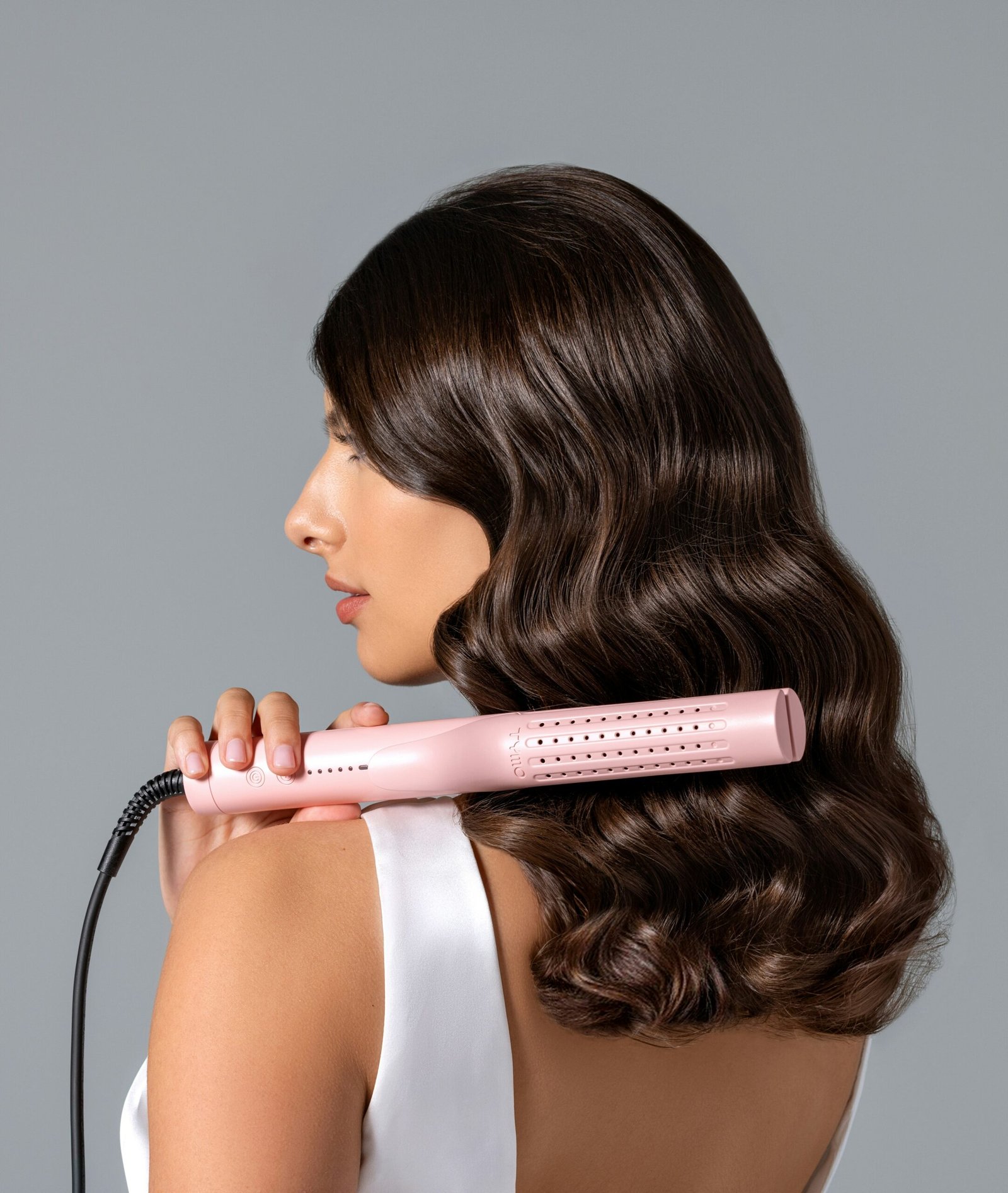 Captured in a moment of elegance, a woman's glossy, curled hair cascades down as she styles it with a TYMO hair curler, an icon of modern hairstyling.