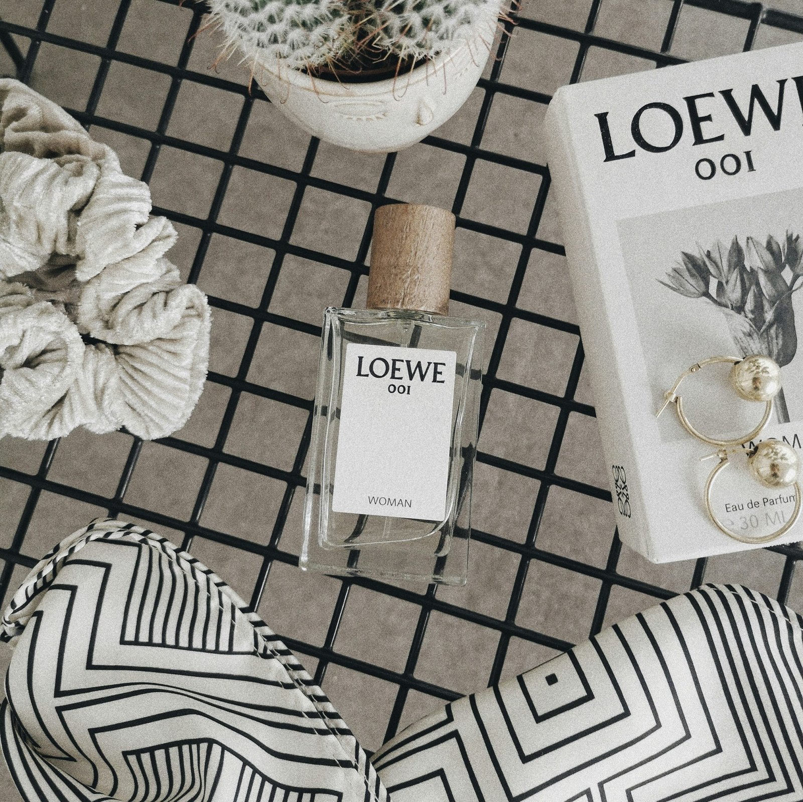 Loewe perfume in a flatlay with gold earrings and a scrunchie.